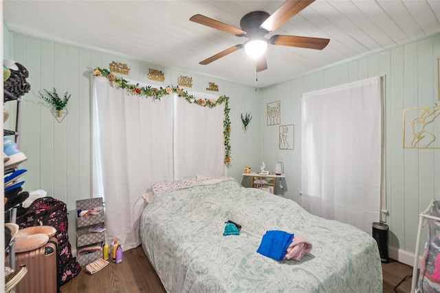 bedroom featuring wooden walls, a ceiling fan, and wood finished floors