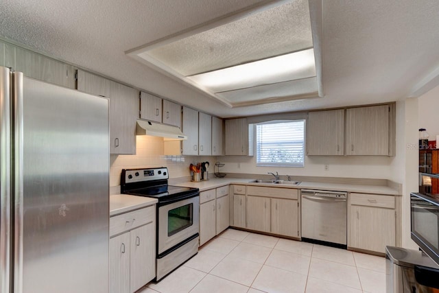 kitchen with appliances with stainless steel finishes, a sink, a raised ceiling, light countertops, and under cabinet range hood