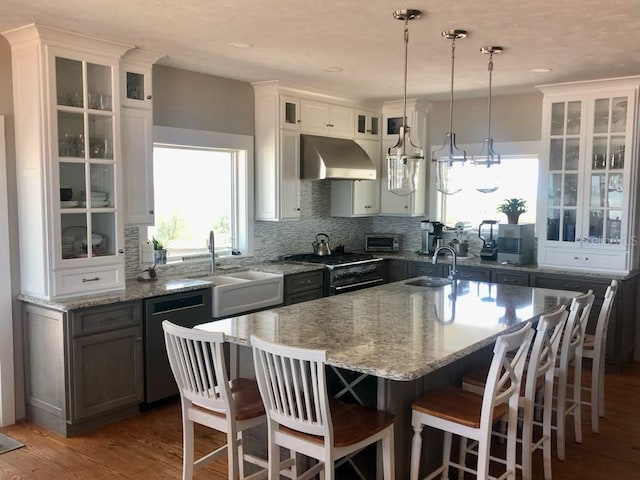 kitchen with a sink, range hood, light stone countertops, and dishwasher