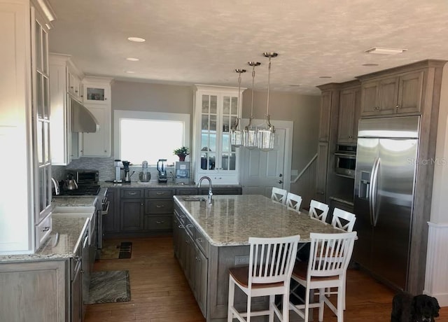 kitchen featuring light stone counters, dark wood finished floors, appliances with stainless steel finishes, and a center island with sink