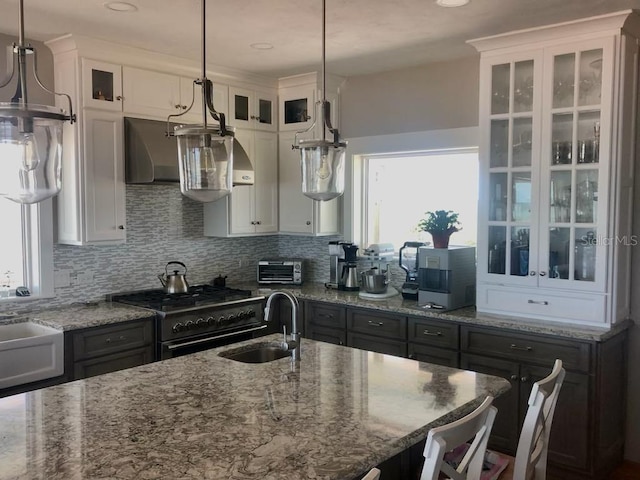 kitchen with gas stove, light stone counters, white cabinets, and a sink