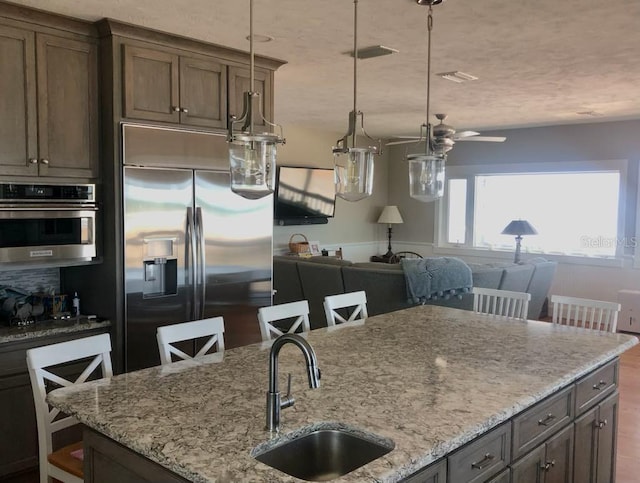 kitchen with a sink, a ceiling fan, stainless steel appliances, and light stone countertops