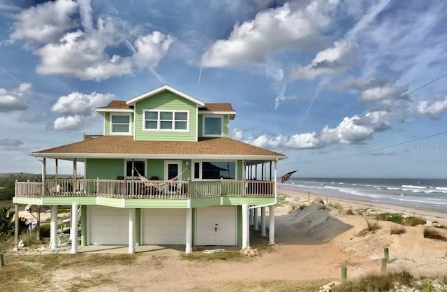 back of property with driveway, roof with shingles, a view of the beach, a garage, and a water view