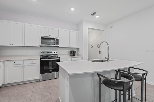 kitchen featuring light tile patterned flooring, a breakfast bar area, light countertops, a sink, and stainless steel appliances