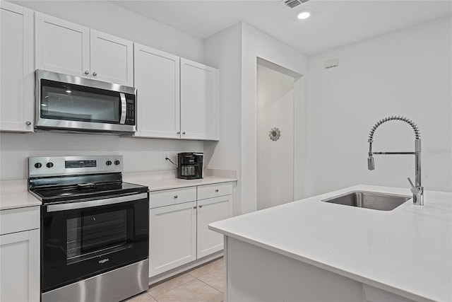 kitchen featuring appliances with stainless steel finishes, a sink, light countertops, white cabinetry, and light tile patterned floors