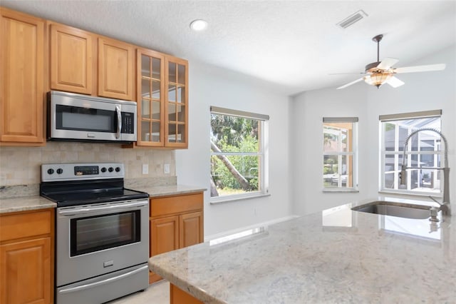 kitchen featuring visible vents, light stone countertops, glass insert cabinets, backsplash, and stainless steel appliances