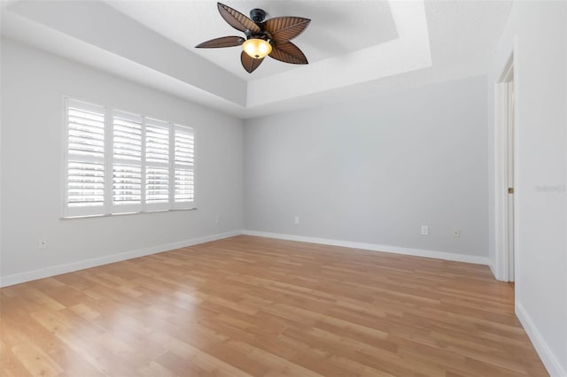 unfurnished room with baseboards, a ceiling fan, light wood finished floors, and a raised ceiling