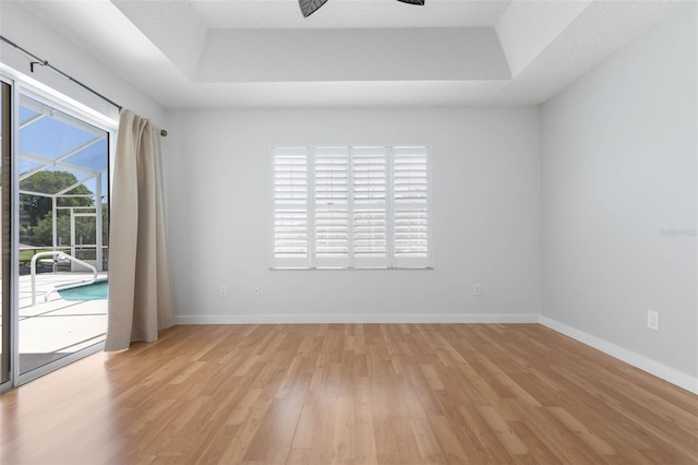 spare room with light wood-type flooring, a raised ceiling, ceiling fan, and baseboards