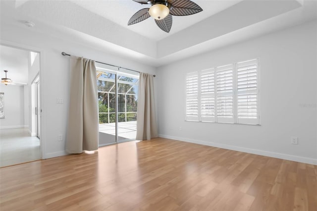 unfurnished room featuring baseboards, light wood finished floors, ceiling fan, and a tray ceiling
