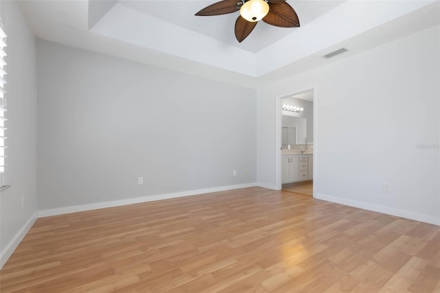 unfurnished bedroom featuring visible vents, a raised ceiling, baseboards, light wood-style floors, and ensuite bathroom