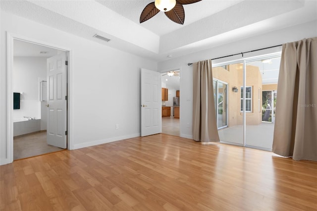 unfurnished bedroom featuring access to outside, light wood finished floors, baseboards, a tray ceiling, and visible vents