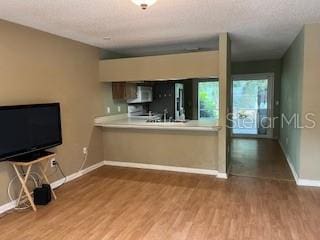 unfurnished living room featuring baseboards, wood finished floors, and a textured ceiling