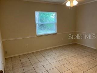 empty room featuring crown molding, light tile patterned floors, ceiling fan, and baseboards