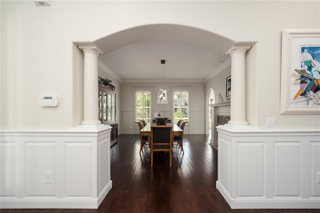 dining area featuring ornate columns, a decorative wall, arched walkways, dark wood-type flooring, and wainscoting