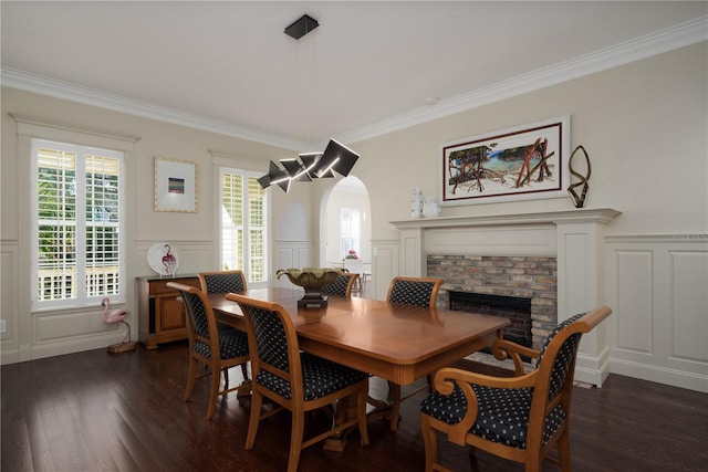 dining area with a decorative wall, a fireplace, dark wood-style flooring, crown molding, and wainscoting