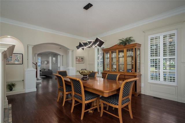 dining room with ornate columns, arched walkways, a decorative wall, crown molding, and dark wood finished floors