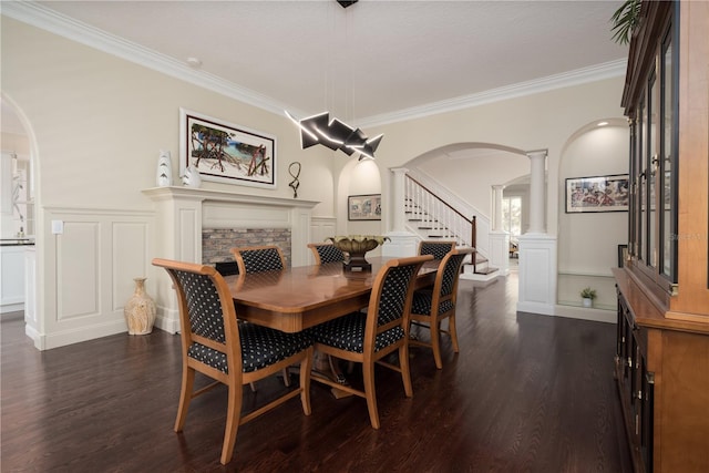 dining room featuring arched walkways, a decorative wall, ornate columns, stairway, and dark wood finished floors