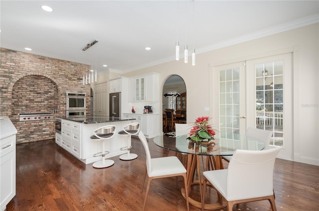 dining area featuring brick wall, arched walkways, dark wood-style flooring, ornamental molding, and recessed lighting