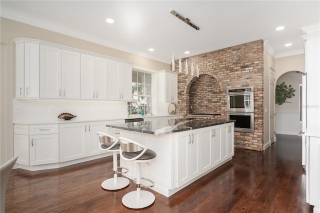 kitchen with double oven, a kitchen island, white cabinets, dark wood finished floors, and ornamental molding