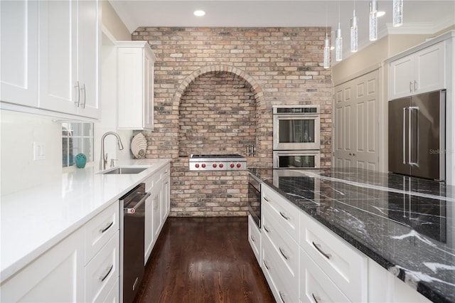 kitchen with a sink, appliances with stainless steel finishes, brick wall, white cabinets, and dark wood-type flooring