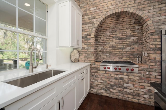 kitchen featuring a sink, stainless steel gas cooktop, brick wall, light countertops, and white cabinetry