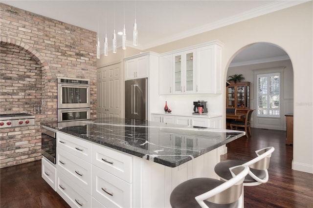 kitchen featuring stainless steel appliances, dark wood-style floors, glass insert cabinets, dark stone countertops, and white cabinetry