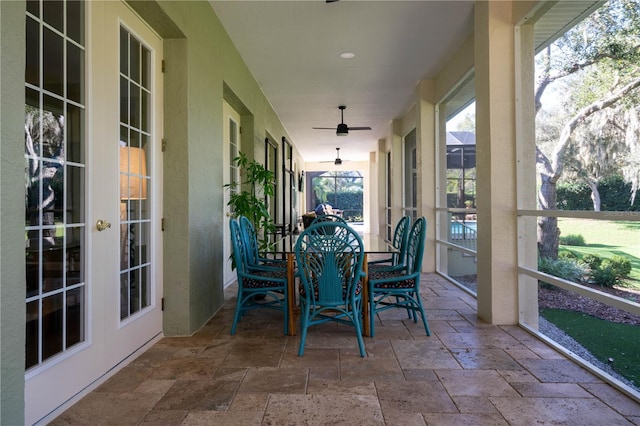 sunroom with stone tile flooring, a ceiling fan, french doors, and outdoor dining space