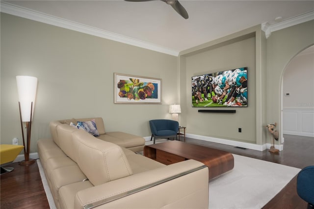 living area featuring dark wood finished floors, a ceiling fan, arched walkways, crown molding, and baseboards
