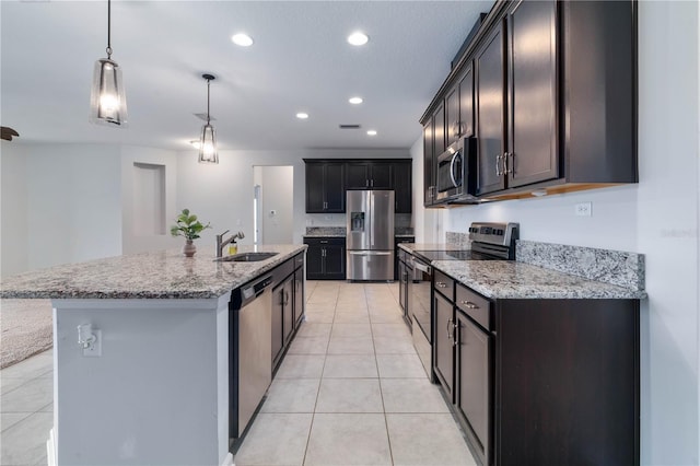 kitchen with stainless steel appliances, a sink, light tile patterned floors, light stone countertops, and a center island with sink