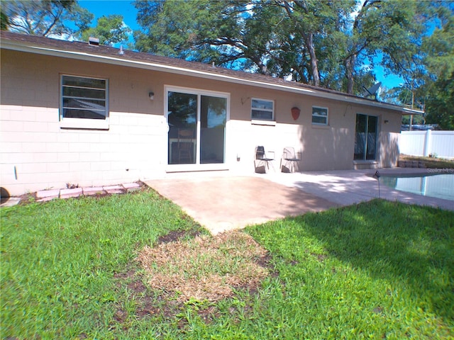 rear view of property featuring a yard, a patio area, concrete block siding, and fence