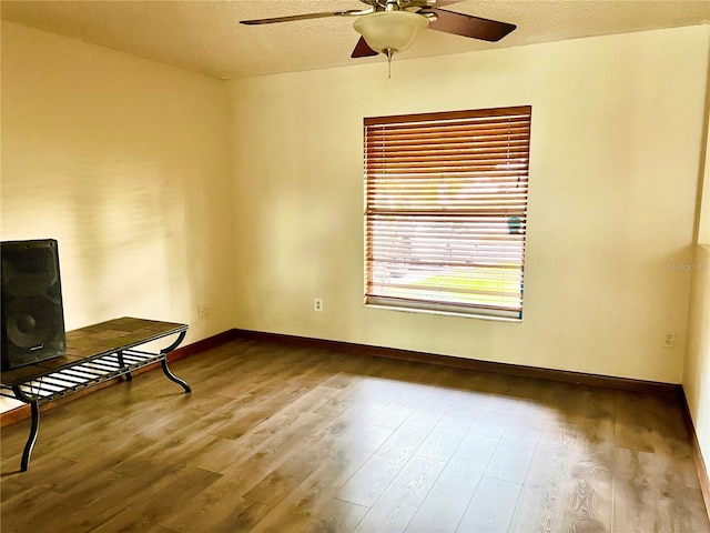 spare room featuring a textured ceiling, baseboards, wood finished floors, and a ceiling fan