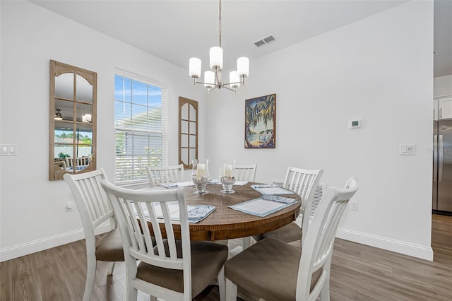 dining room featuring visible vents, wood finished floors, baseboards, and a notable chandelier