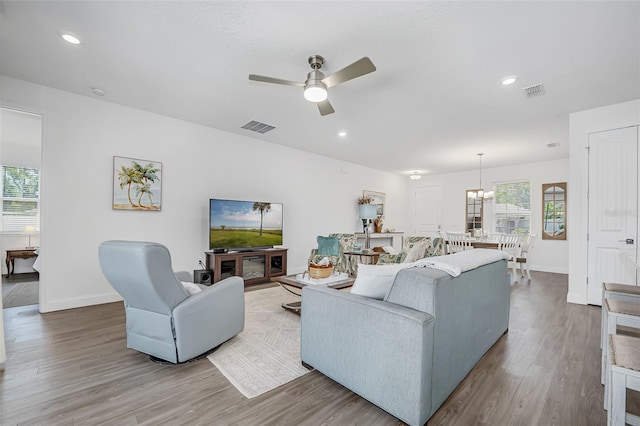 living room featuring ceiling fan with notable chandelier, baseboards, visible vents, and wood finished floors