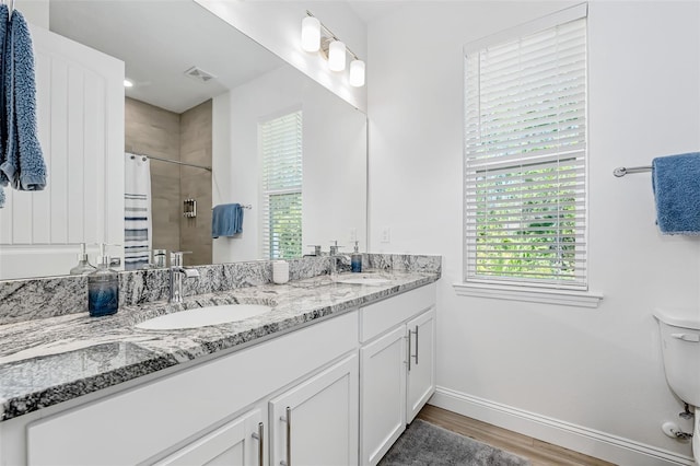 full bath with a tile shower, plenty of natural light, a sink, and wood finished floors
