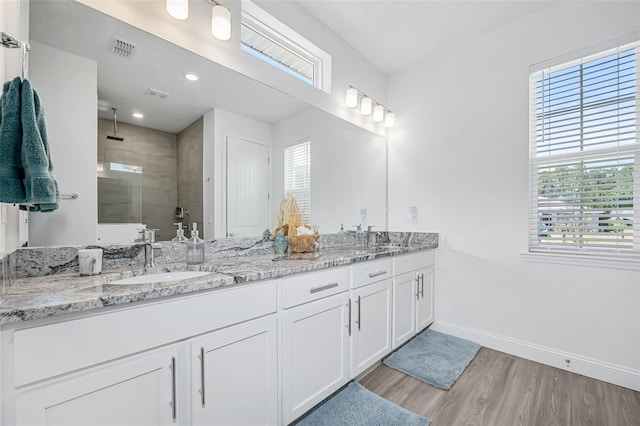 full bath featuring wood finished floors, tiled shower, a sink, visible vents, and baseboards