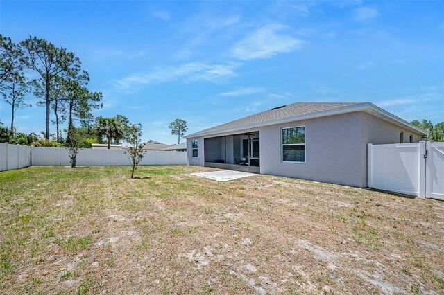 back of property featuring a gate, stucco siding, a fenced backyard, a lawn, and a sunroom