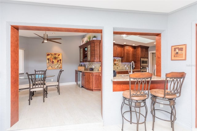 kitchen featuring a ceiling fan, backsplash, light wood-type flooring, a breakfast bar, and stainless steel appliances