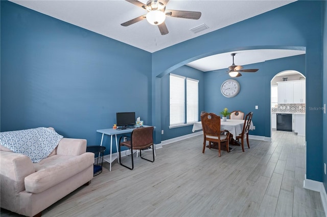 office with visible vents, light wood-style floors, baseboards, arched walkways, and a ceiling fan
