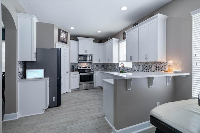 kitchen featuring decorative backsplash, a kitchen bar, light wood-type flooring, light countertops, and stainless steel appliances