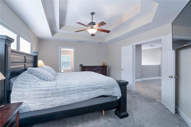 bedroom featuring visible vents, light carpet, baseboards, a tray ceiling, and a ceiling fan