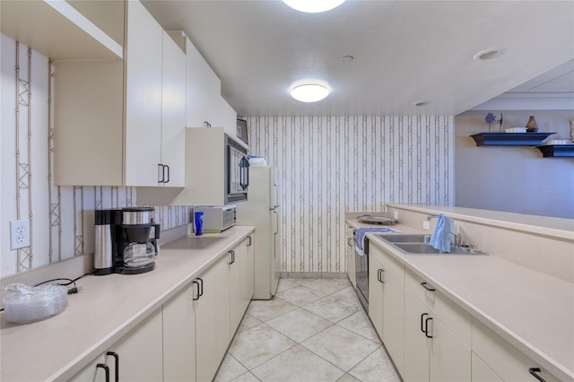 2937 S Atlantic Ave Unit 2001, Daytona Beach, FL 32118 - kitchen with freestanding refrigerator, wallpapered walls, white cabinetry, light countertops, and black microwave