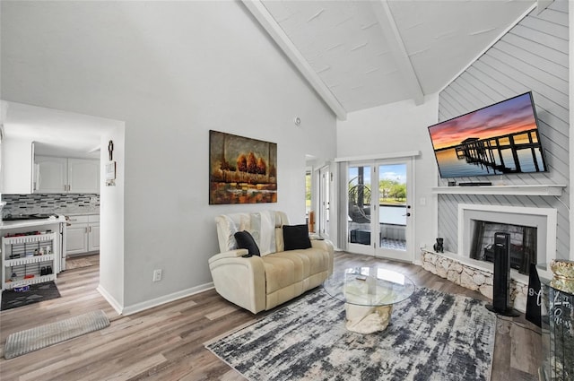 living area with beam ceiling, light wood-style floors, baseboards, high vaulted ceiling, and a fireplace with raised hearth