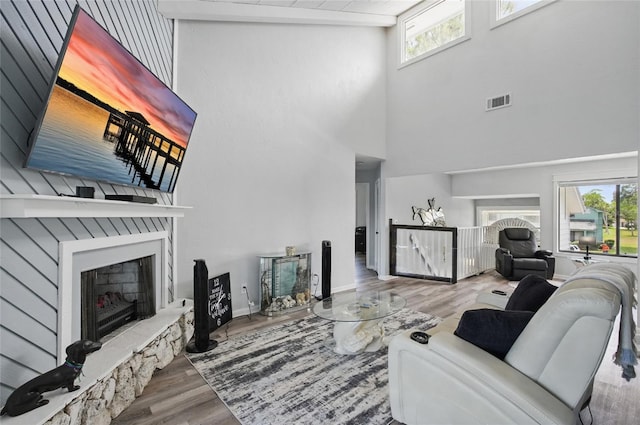 living area with plenty of natural light, a fireplace with raised hearth, wood finished floors, and a towering ceiling