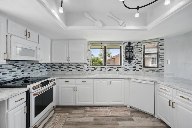 kitchen with a sink, a raised ceiling, decorative backsplash, and white appliances