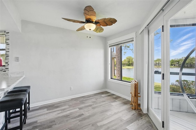 unfurnished dining area featuring light wood-style floors, baseboards, a water view, and ceiling fan
