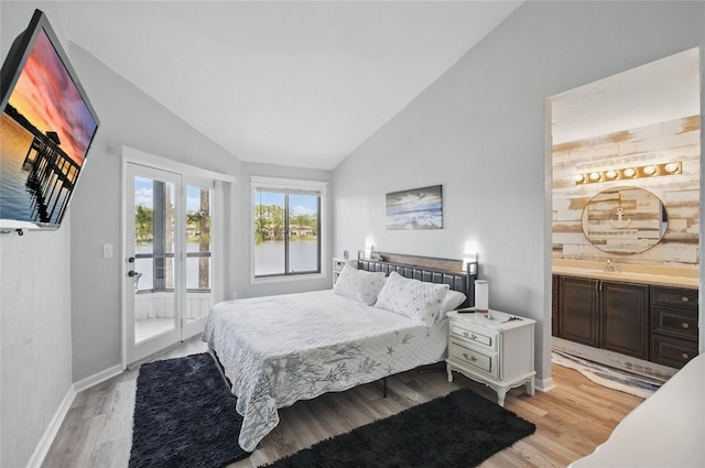 bedroom with baseboards, a sink, light wood-style flooring, ensuite bath, and vaulted ceiling