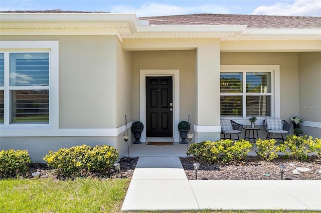 entrance to property with a shingled roof, a porch, and stucco siding