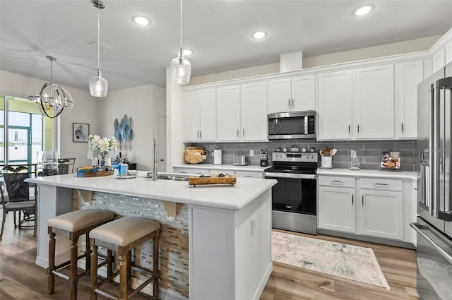 kitchen with appliances with stainless steel finishes, white cabinetry, decorative backsplash, light countertops, and an island with sink