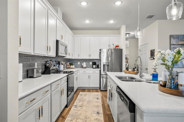 kitchen with a sink, appliances with stainless steel finishes, white cabinets, light countertops, and light wood-style floors