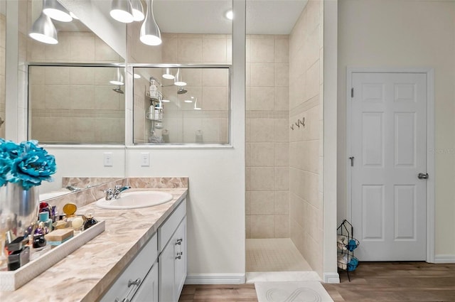 bathroom featuring a tile shower, baseboards, vanity, and wood finished floors